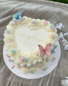 a heart shaped cake sitting on top of a table next to white flowers and butterflies