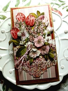 a card with flowers on it sitting on a table next to a white plate and green leaves