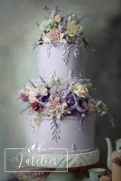 a three tiered cake decorated with flowers and lavenders on a table next to a teapot