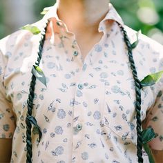 a woman wearing a white shirt with green leaves on the collar and black braids around her neck