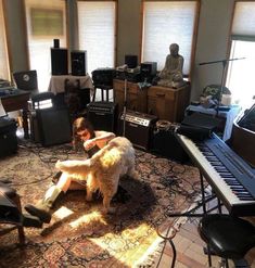 a man sitting on the floor with his dog in front of him and many other musical instruments behind him