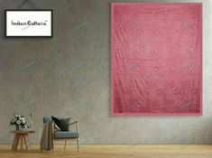 a living room with a chair, table and large pink wall hanging on the wall