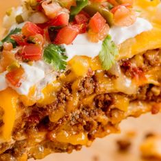 a piece of mexican casserole with sour cream and salsa on top is held up to the camera