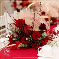 a bouquet of red roses and greenery sits on a table next to a fan