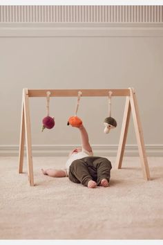 a baby laying on the ground in front of a wooden frame with balls hanging from it