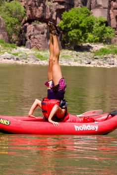 a man is doing a handstand on top of a red kayak in the water