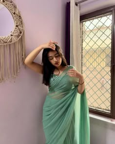 a woman standing in front of a window wearing a green sari and posing for the camera