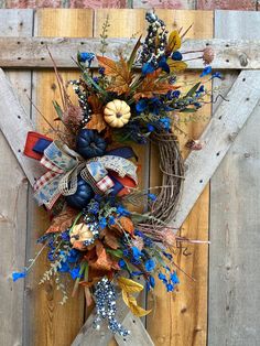 a wreath is hanging on the side of a wooden door with fall decorations and leaves