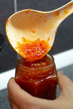 a person is holding a spoon over a jar filled with jam and orange peels