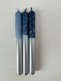 three blue and silver candles sitting next to each other on a white surface with tiny stars