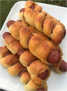 several hot dogs wrapped in bread on a white plate with grass in the back ground