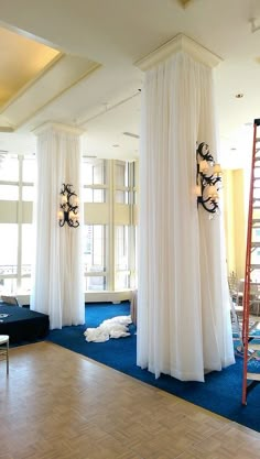 an empty room with blue carpet and white drapes on the walls, two ladders hanging from the ceiling