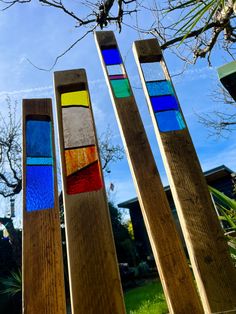 four wooden poles with different colored stained glass pieces on them in front of a tree