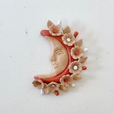 a ceramic sun and moon with flowers on it's face is mounted to the wall