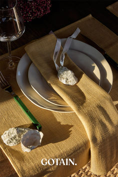 A Christmas table setting featuring mustard woven linen napkins, dried floral centerpieces with ribbon, and rustic decor on a wooden table.