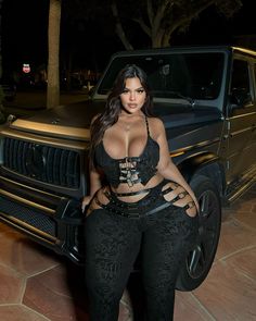 a woman posing in front of a black truck with her hands on her hips and wearing high heels