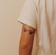 a person with a tattoo on their arm pointing at the creation of a human hand