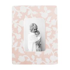 a woman holding a baby in front of a white floral wallpaper pattern with a black and white photo frame