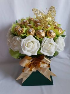 a bouquet of white roses and chocolates in a green box with a gold butterfly on top