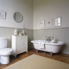 a white bath tub sitting next to a toilet in a bathroom under a round mirror