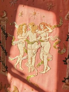 an embroidered cloth with three cherubs in gold and pink colors on a red background