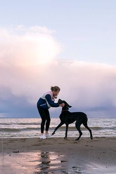 a woman is playing with her dog on the beach at sunset by helen happle for stockstation