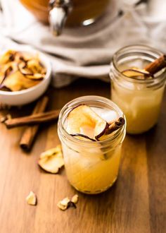 two mason jars filled with apple cider and cinnamon on top of a wooden table