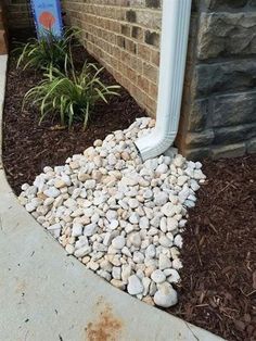 a white pipe sticking out of the ground next to a flower bed with rocks and mulch