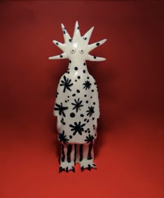 a ceramic figurine with black and white designs on it's body, standing in front of a red background