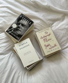 three books sitting on top of a bed next to each other in front of a white sheet