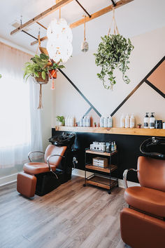 Caramel-colored shampoo systems with black wash bowls stand in front of a product display mounted on an eclectic wall. Salon Shampoo Bowl Area, Boho Salon Station Ideas, Salon Washing Station Ideas, Salon Suite Shampoo Area, Shampoo Back Bar Ideas Salon, Suite Salon Ideas, Hair Salon Shampoo Area Ideas, Salon Suite Layout, Shampoo Area In Salon