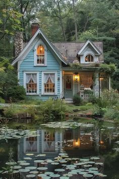 a blue house sitting next to a pond with lily pads on the ground and trees in the background