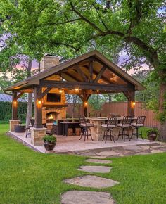 an outdoor kitchen and grill area in the middle of a yard with grass, rocks and trees