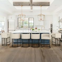 a large kitchen with an island in the middle and white chairs around it, along with lots of windows