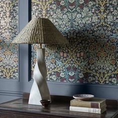 a lamp sitting on top of a wooden table next to a wallpapered wall