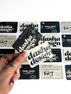 someone holding up some business cards in front of a wall of stickers that say, dasha design