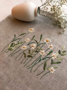 some white flowers and green stems on a linen table cloth next to a vase with water in it