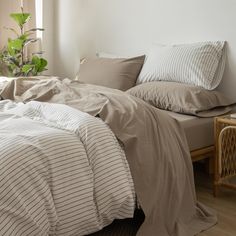 an unmade bed with two pillows on top of it next to a table and chair