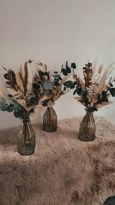 three vases filled with dried flowers on top of a blanket