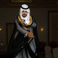 a man dressed in black and gold is standing with his hands on his hips while wearing a white headdress