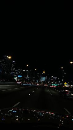 the city lights shine brightly in the dark night time sky over an empty highway with cars driving on it