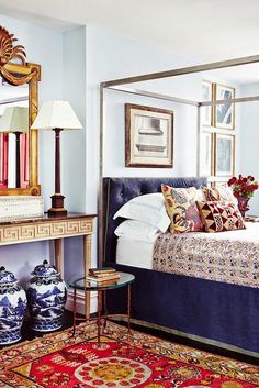 a bed sitting in a bedroom next to a mirror and table with vases on it