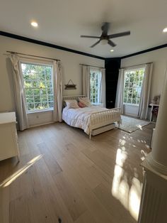 a large bedroom with hardwood floors and white walls, has two windows that look out onto the backyard