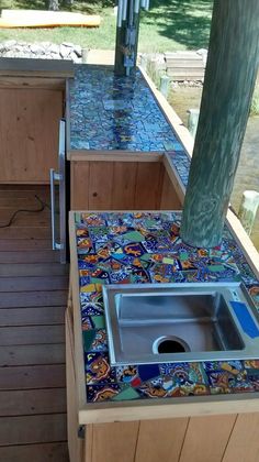 an outdoor kitchen with colorful tiles on the counter tops and flooring, as well as a stainless steel sink