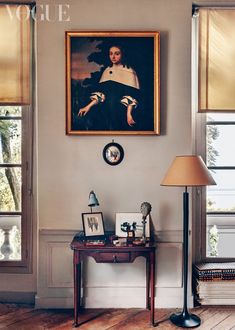 a painting hangs on the wall next to a lamp and table with pictures in it