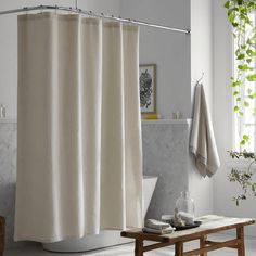 a bathroom with a white shower curtain next to a bathtub and a wooden bench