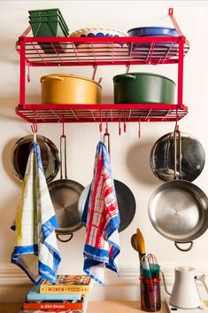 pots and pans are hanging on the wall above a shelf with cookbooks, utensils, and other kitchen items