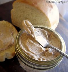 peanut butter in a glass jar with a spoon next to some bread on a table