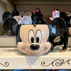 mickey mouse mugs are lined up on the shelf in front of other merchandise items