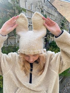 a woman with her hands on her head wearing a knitted bunny ears hat and sweater